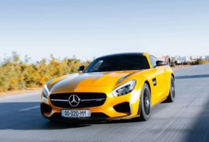 A yellow Mercedes-Benz sports car driving on a highway under a clear blue sky